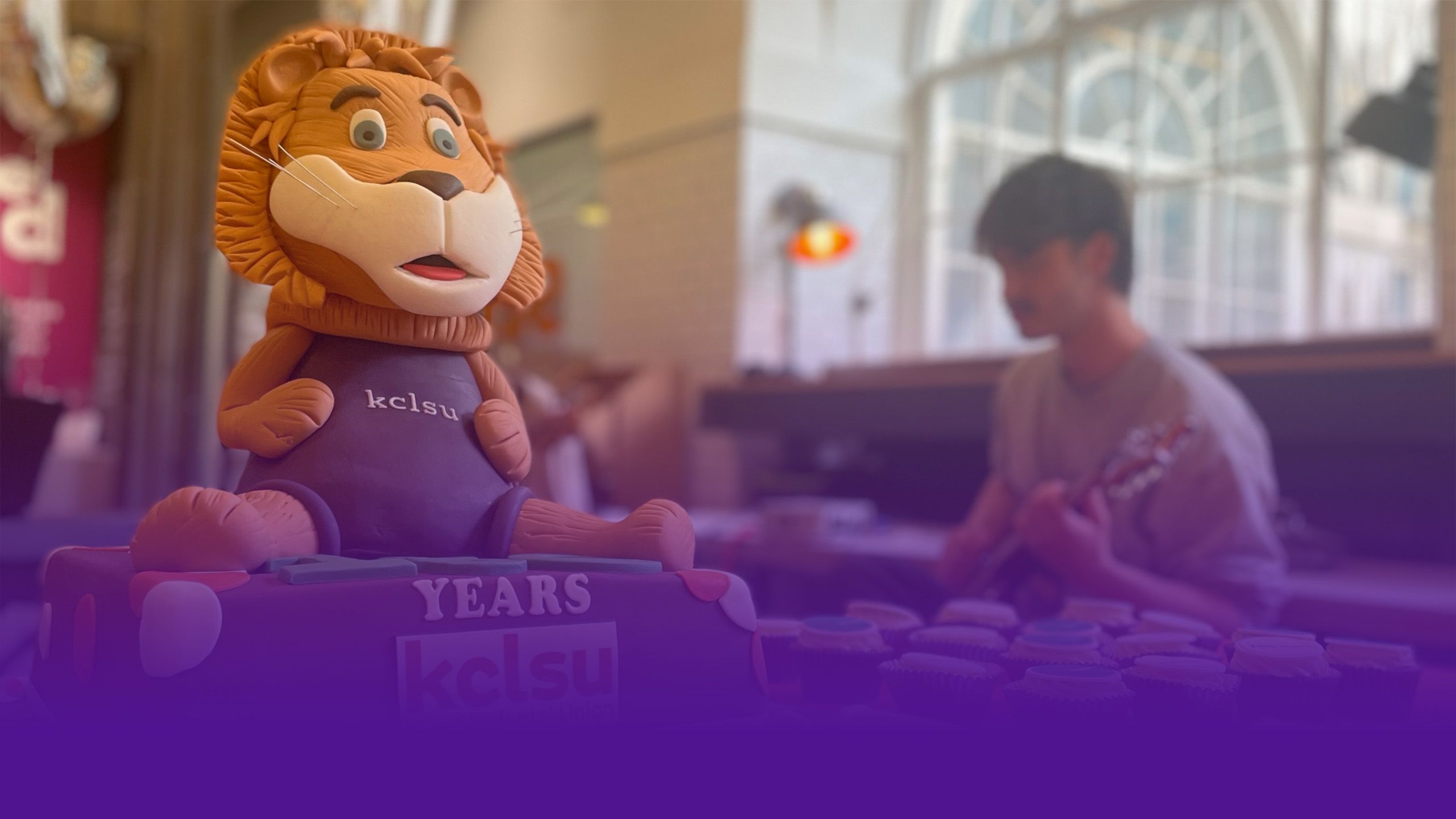 A cake featuring the King's College London mascot Reggie is pictured in front of a guitarist.