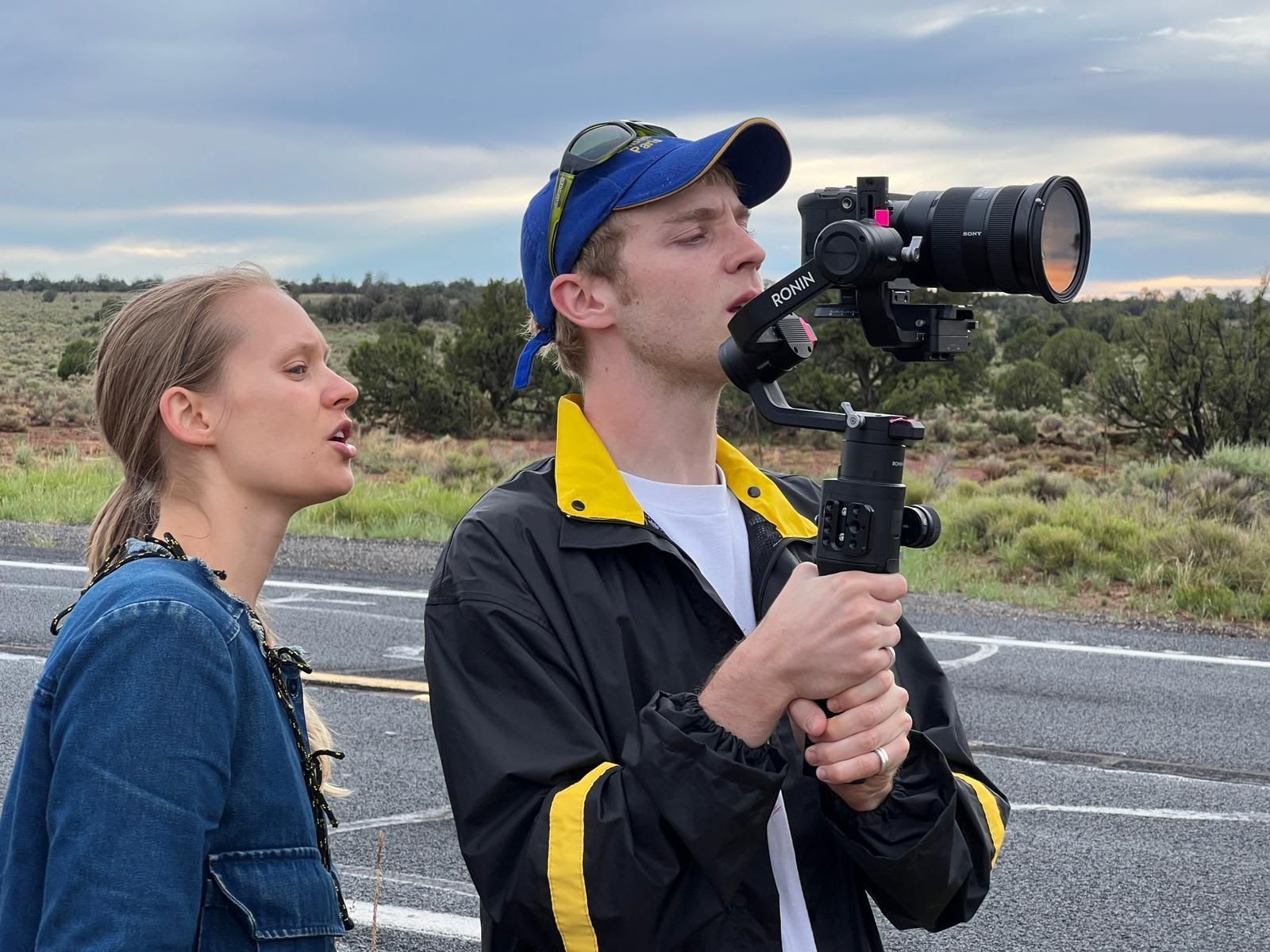 Sophie Compton and Reuben Hamlyn are pictured planning a shot by the roadside. Reuben is holding a camera on a handheld tripod.
