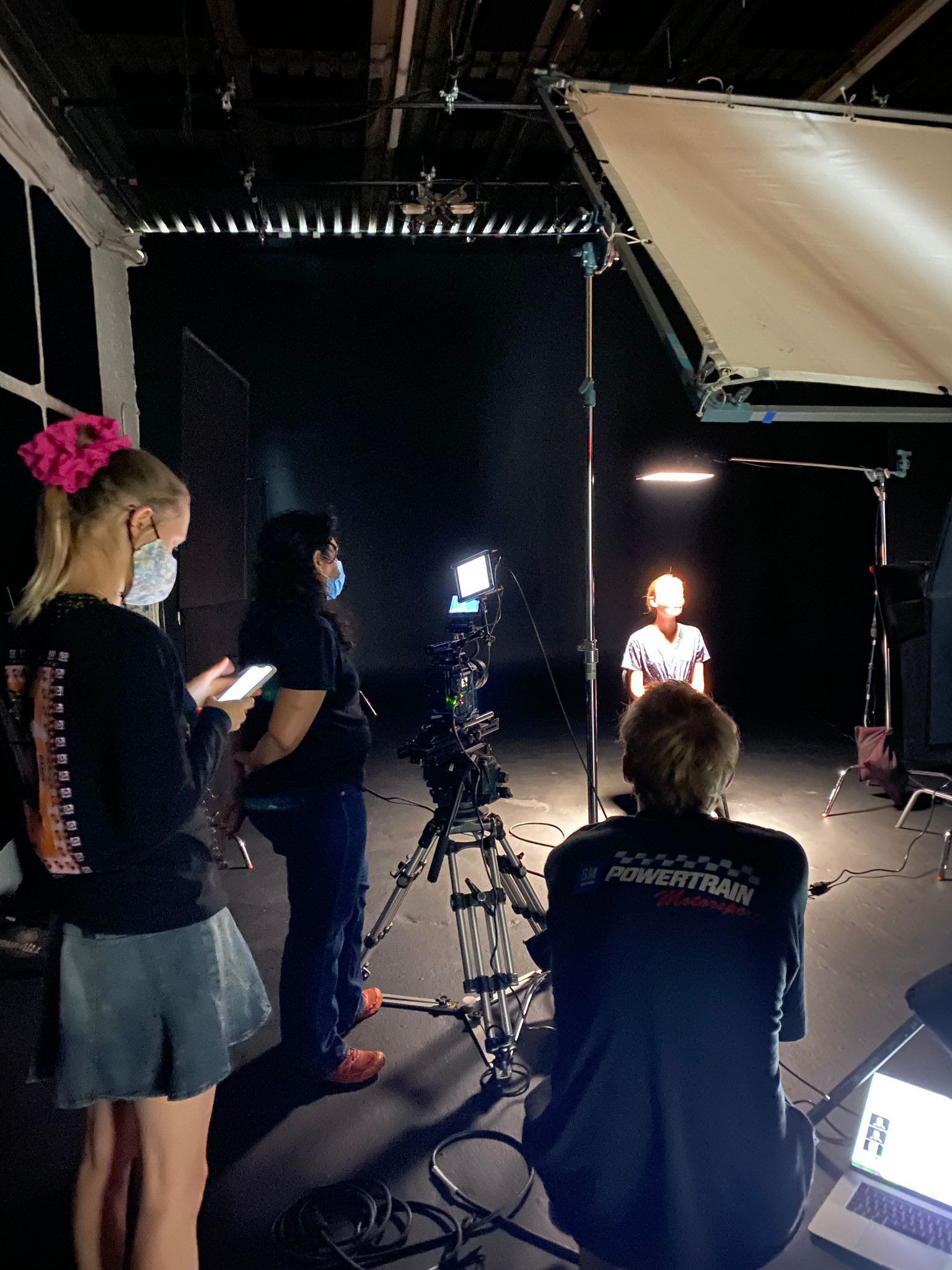 A woman has her face washed out in bright light whilsrt being interviewed for the documentary. The crew can be seen.