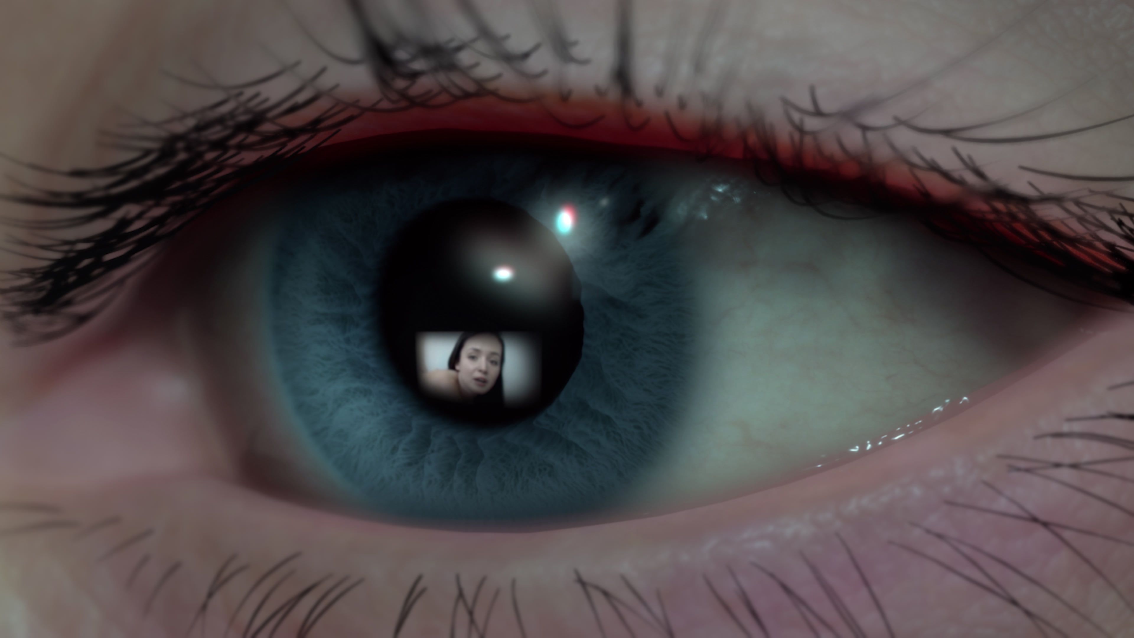 A close up of a blue eye watching a screen. The reflection in the eye shows a woman.