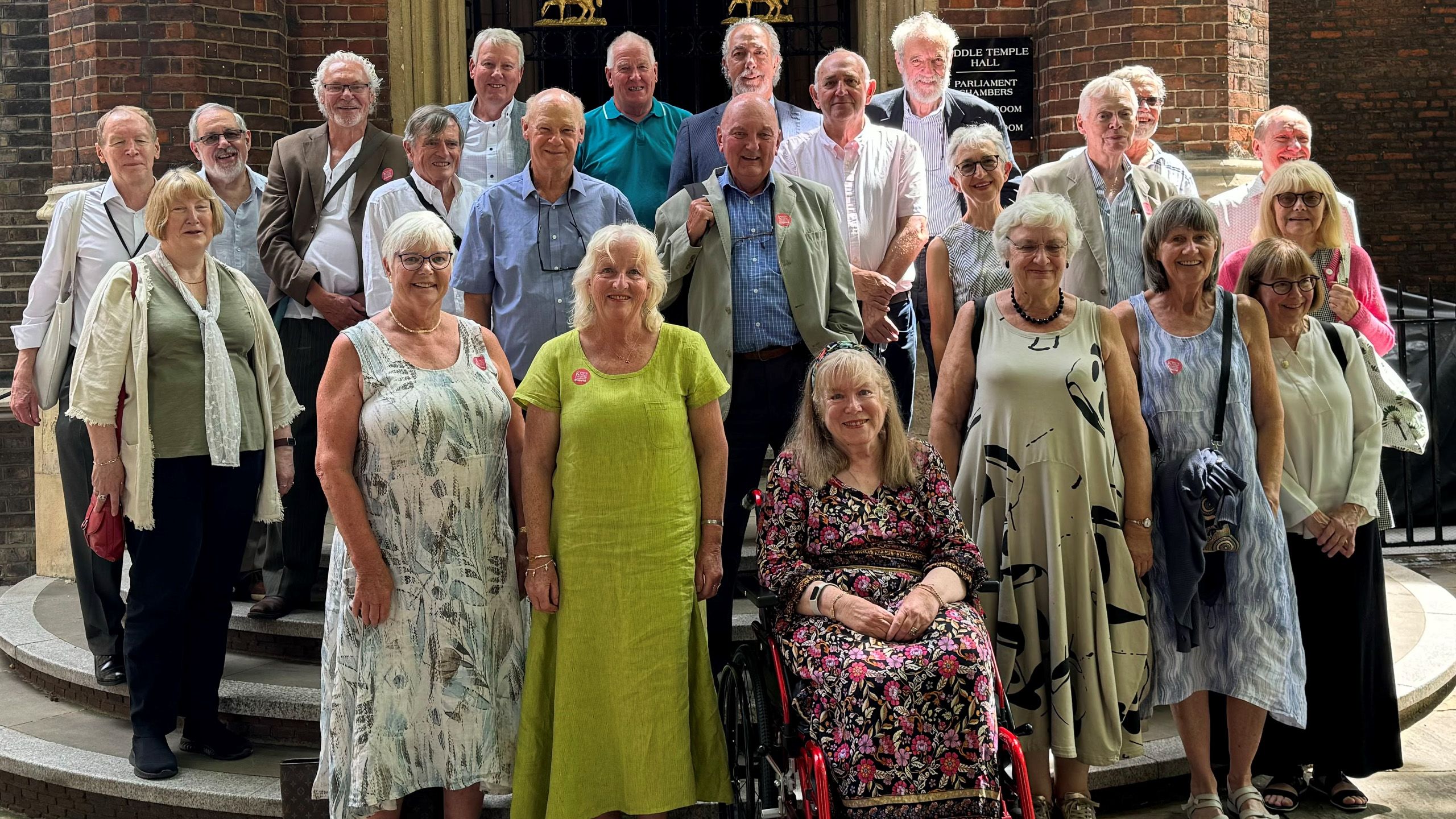 Over 20 members of the Geography class of 1974 smile in the sunshine.