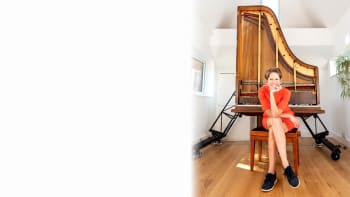 Sarah Nicolls sits in front of her innovative vertical piano. She is wearing an orange dress.