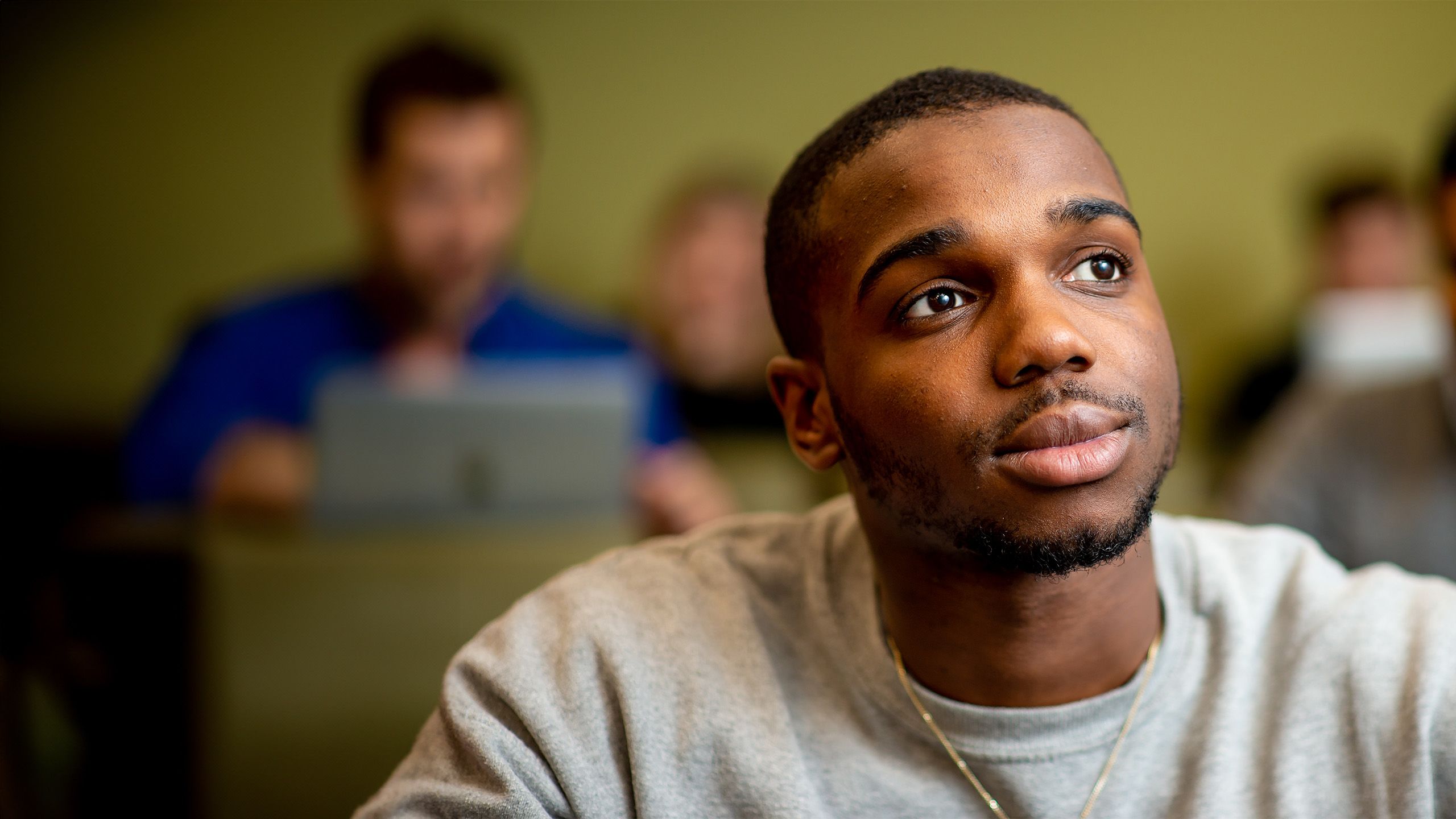 A young student stares into the middle distance. He is wearing a white sweatshirt