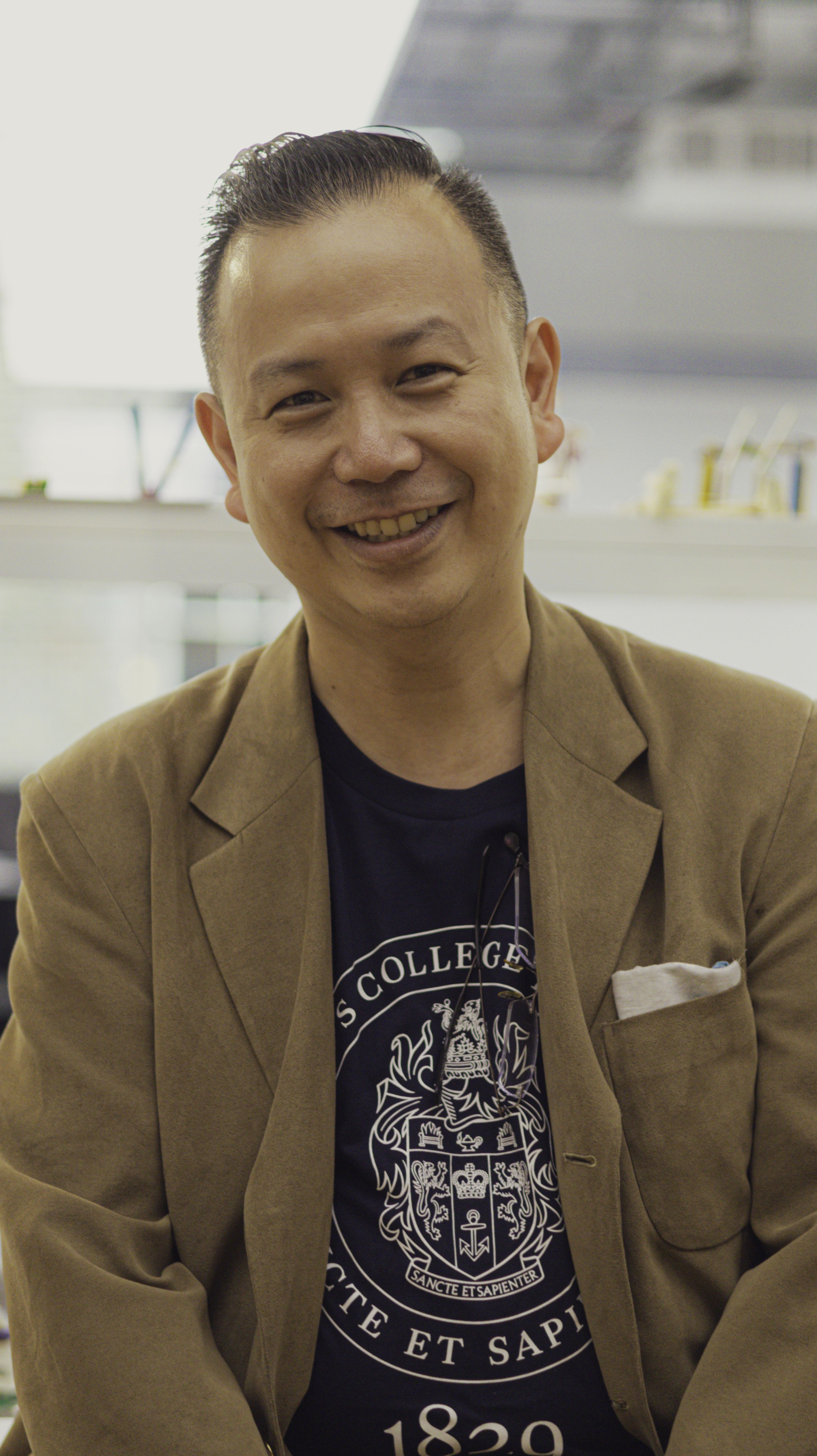 Another shot of Dr Gerald Ariff smiling in front of the engineering labs at King's. His Tshirt is now visible, which has the King's College London crest on it.