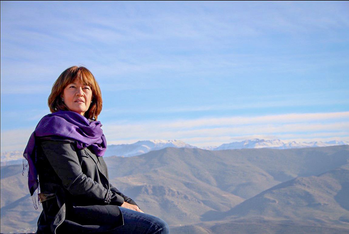 Jane Corbin standing in front of a mountainous landscape under a clear sky.