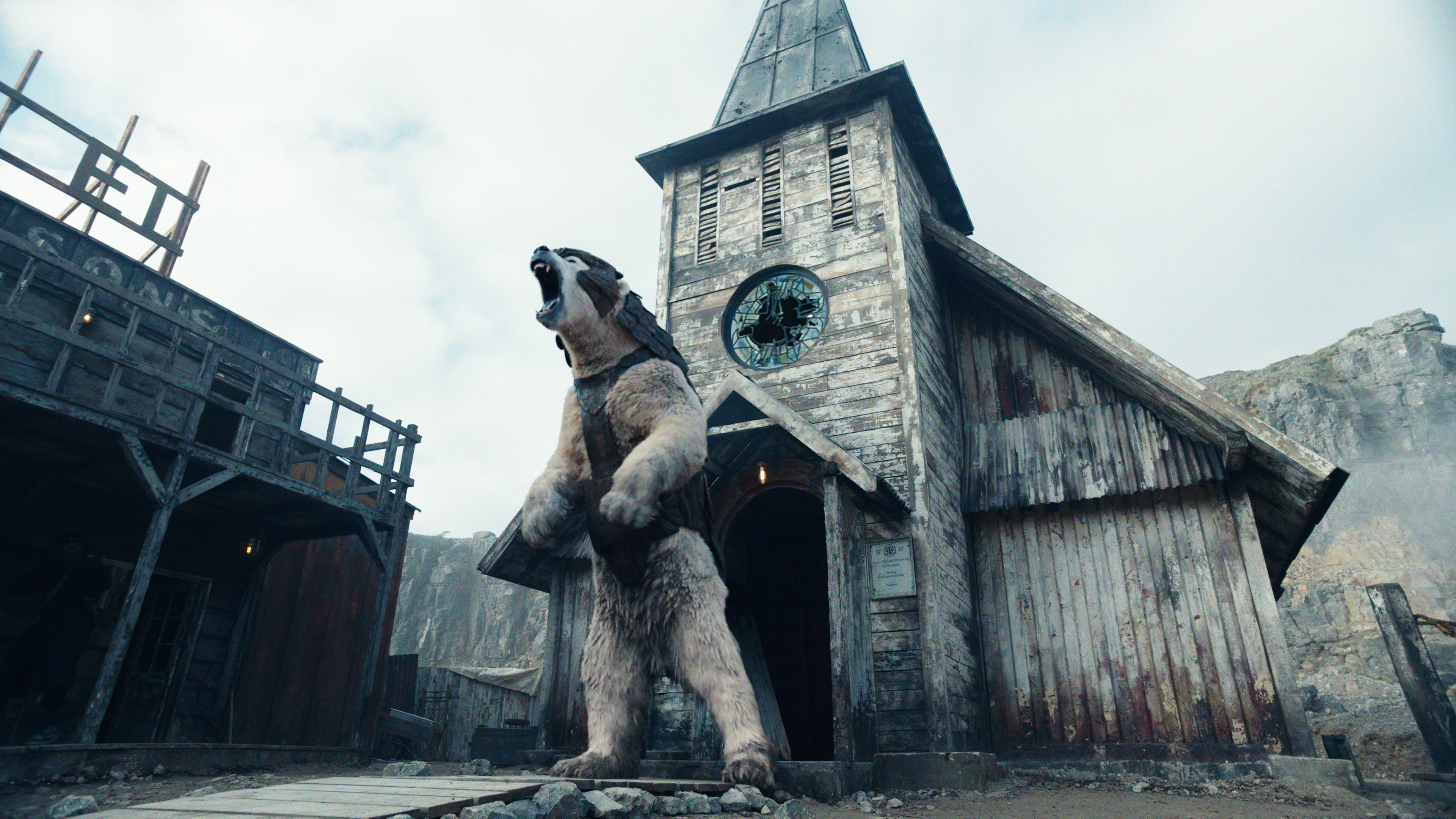 A still image from His Dark Materials. A large beast roars on its hind legs in front of a small church.