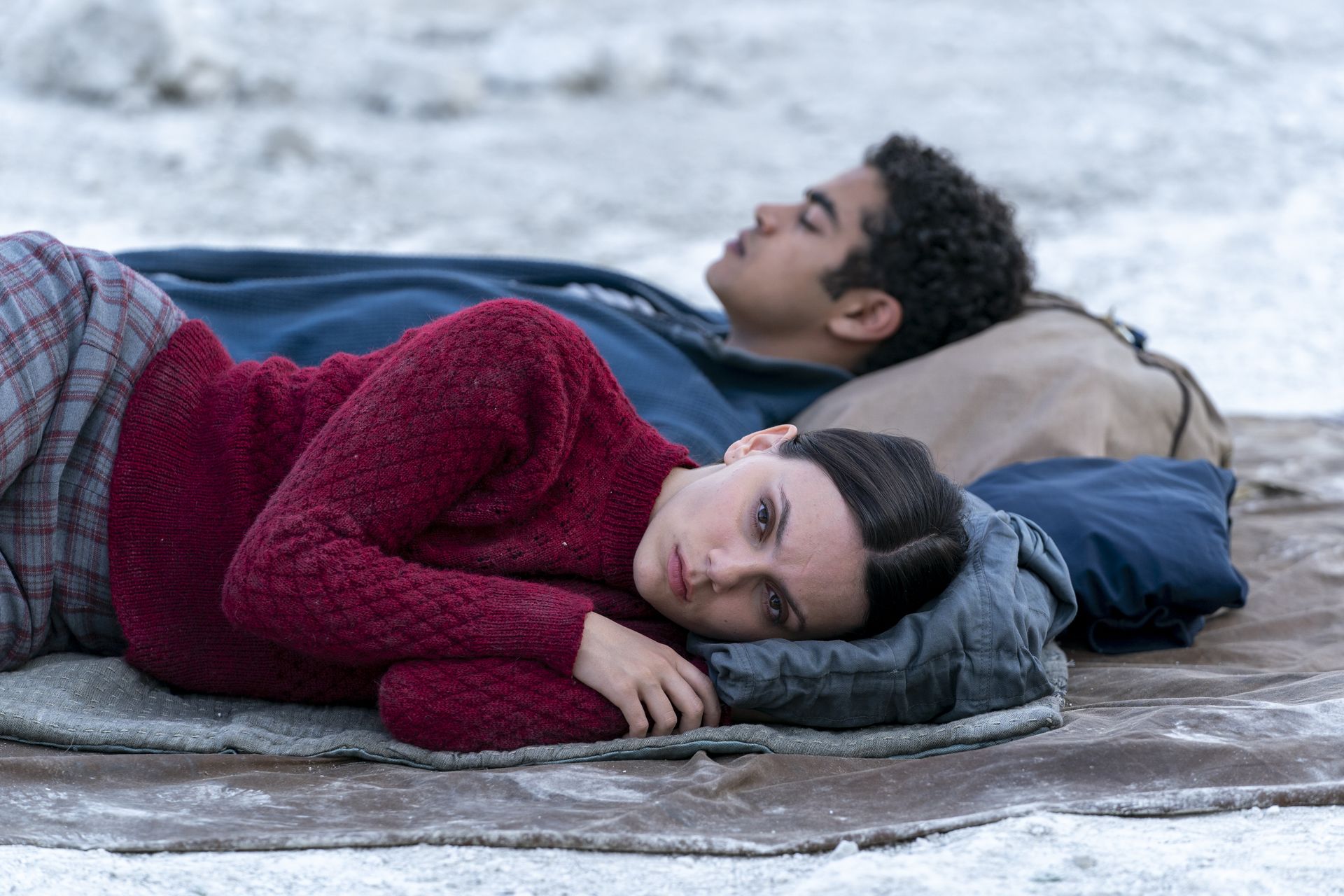 A young woman and a young man lie on the frosted ground. They are not looking at each other. It is a production still from Jane's version of 'His Dark Materials'.