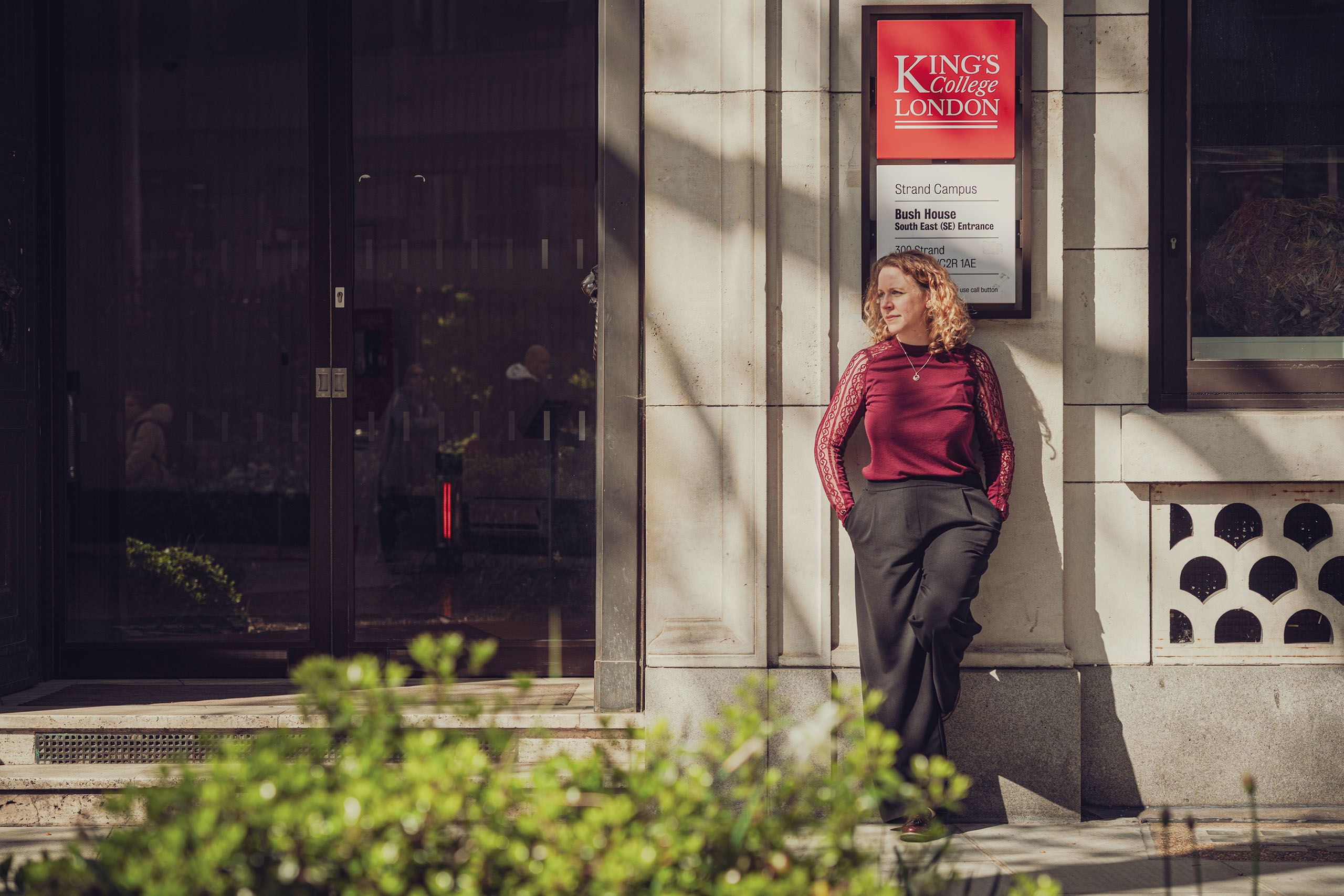 Emma leans against a wall at Bush House looking off into the distance.