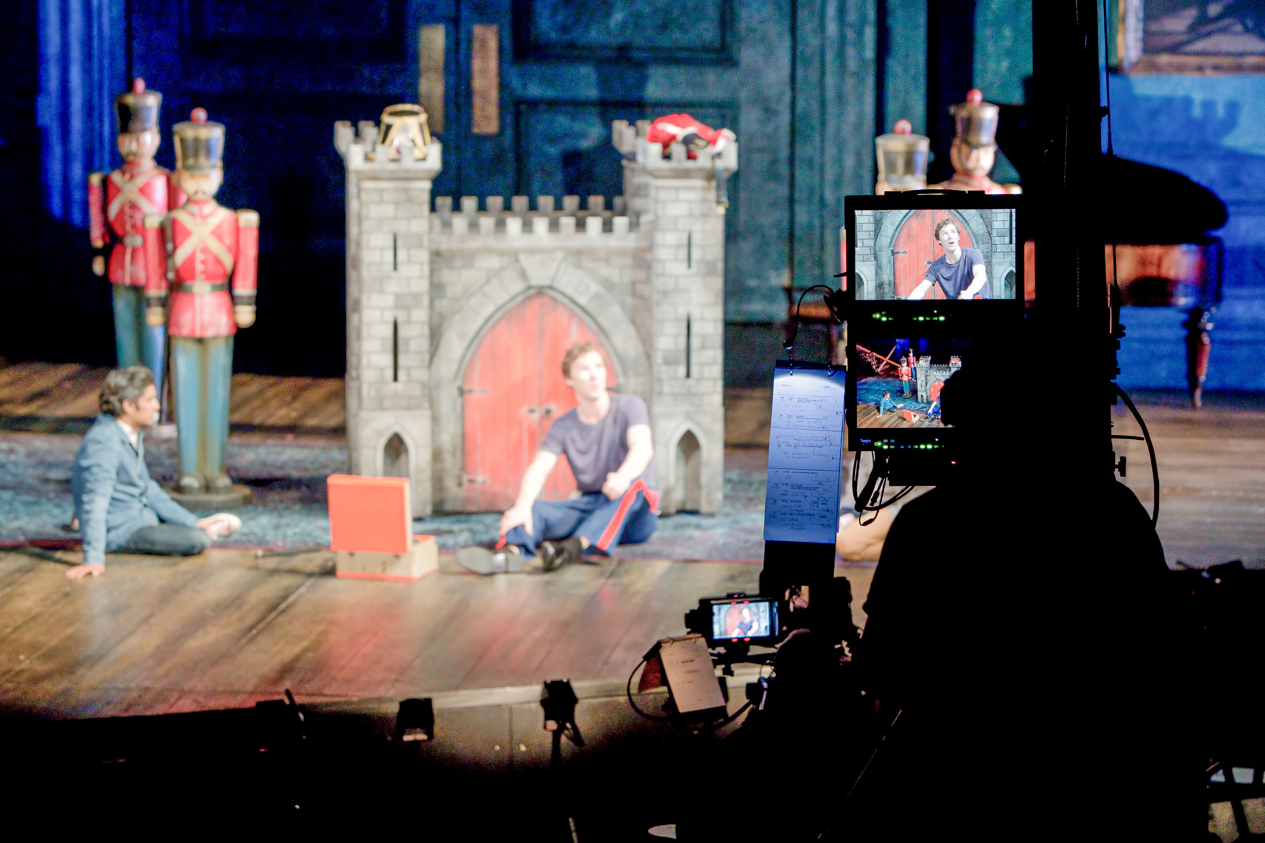 A video camera in focus on a theatre set, filming Benedict Cumberbatch, who is blurred in the background.