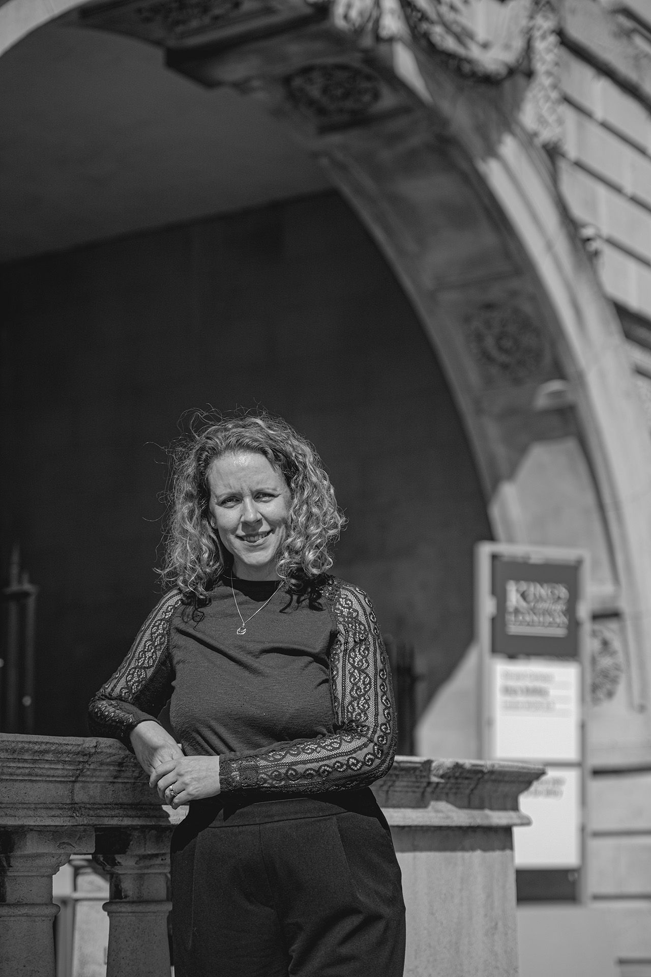 Emma Keith, pictured in black and white, looking at the camera while leaning on a stone pillar on the Strand Campus.