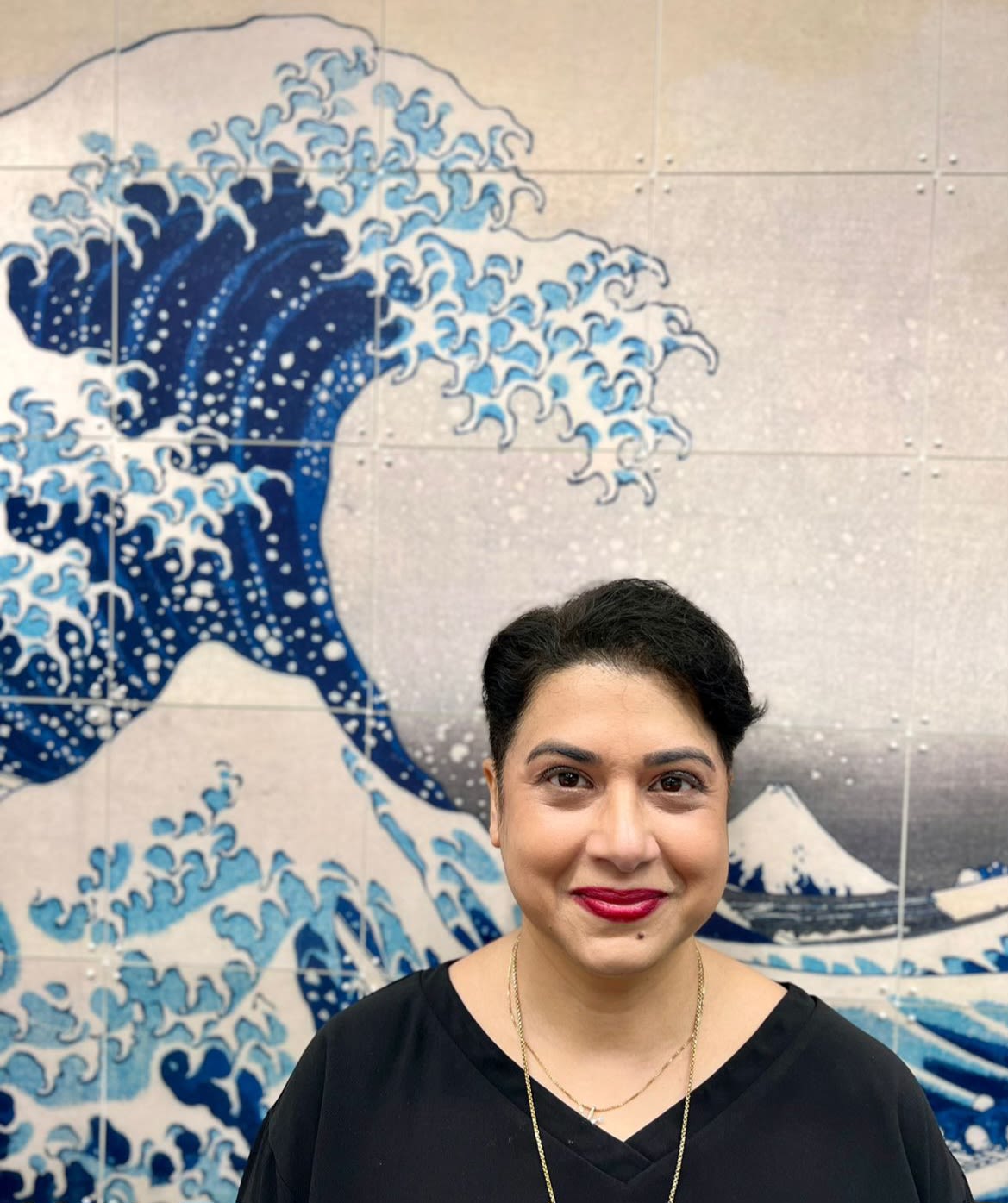 Dr Monica Malik is pictured standing in front of a print of the painting entitled 'The Great Wave off Kanagawa' by Katsushika Hokusai 