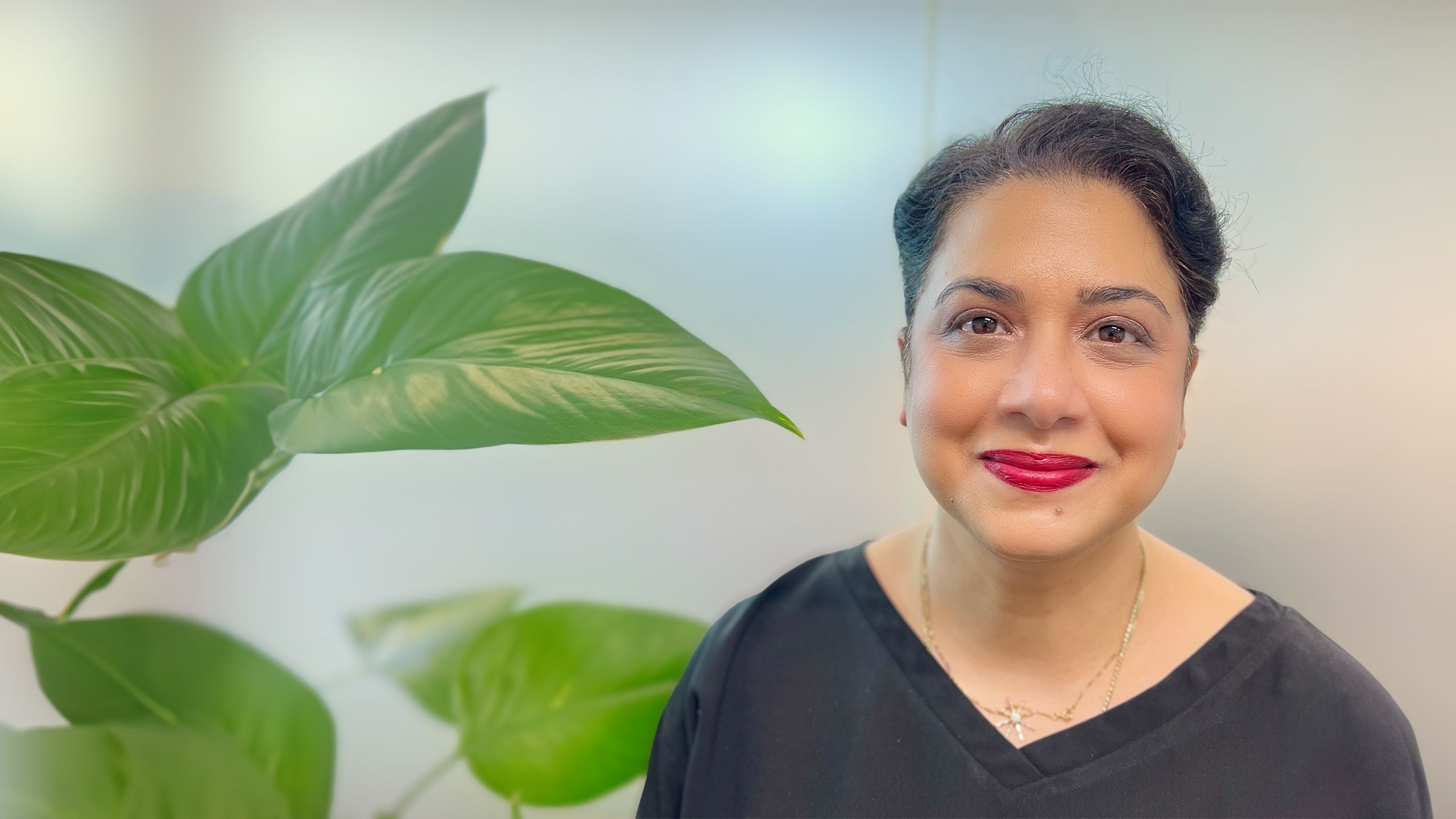 Dr Monica Malik smiles in a black top and silver necklace