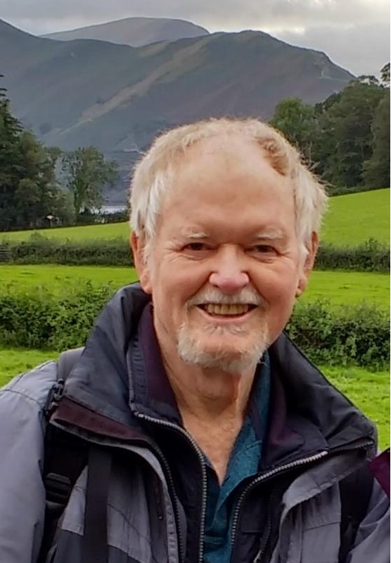 Dr Victor Lewis smiles warmly. He is in the countryside with mountains framing him.