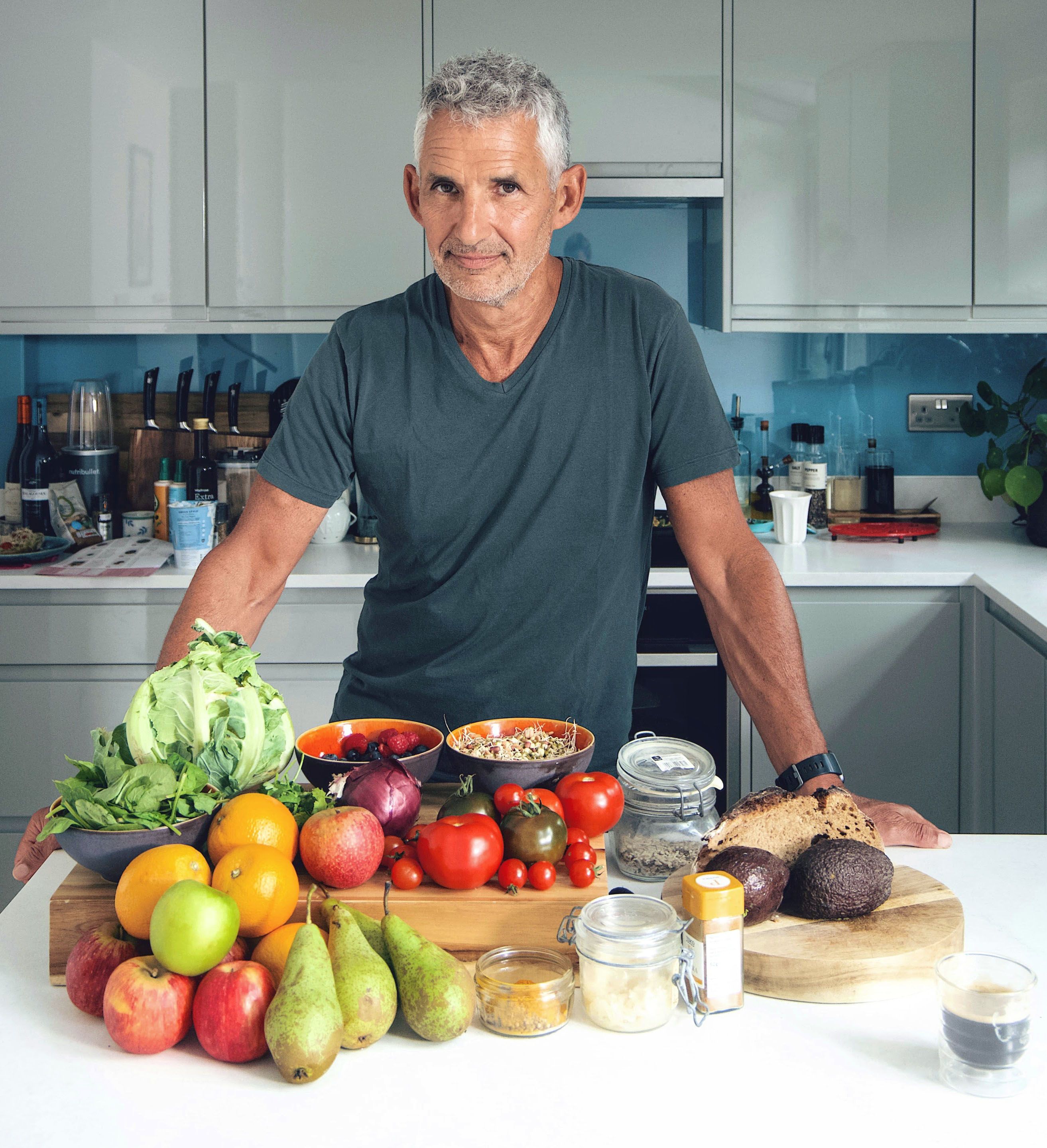 Tim is standing in a kitchen. In front of him is an array of fruit and vegetables.