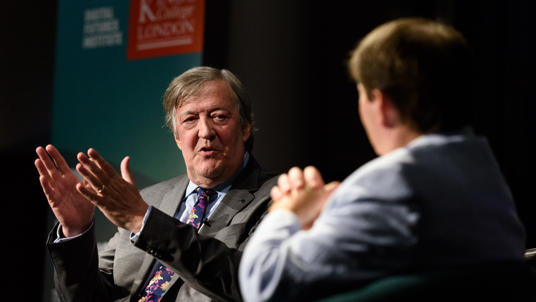 Stephen Fry is pictured in a suit and tie speaking with Dr Marcus Weldon