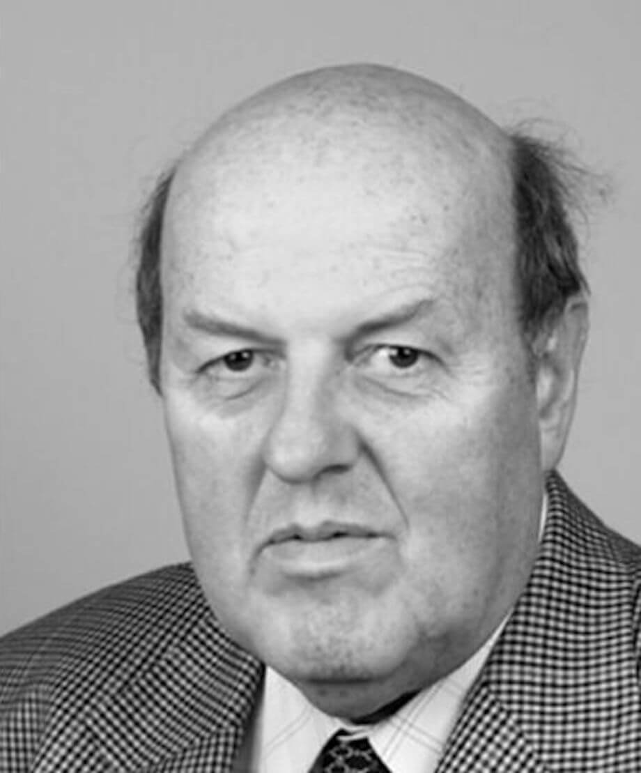 Black and white headshot of a bald man in a tweed jacket
